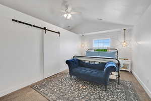 Bedroom featuring carpet flooring, vaulted ceiling, a barn door, and ceiling fan