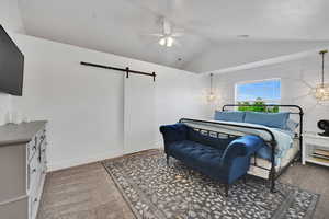 Bedroom featuring vaulted ceiling, a barn door, carpet, and ceiling fan
