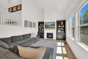 Living room with high vaulted ceiling, wood finished floors, a large fireplace, and recessed lighting