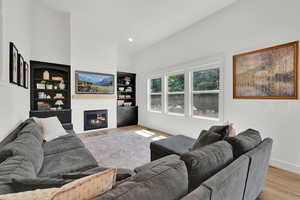 Living room with wood finished floors, a fireplace, high vaulted ceiling, and recessed lighting
