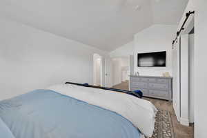 Carpeted bedroom with a barn door, vaulted ceiling, and arched walkways