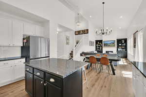 Kitchen with freestanding refrigerator, light wood finished floors, high vaulted ceiling, white cabinets, and open floor plan