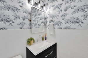 Half bath with wallpapered walls, vanity, wainscoting, and tile walls