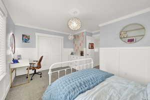 Bedroom featuring carpet, wainscoting, ornamental molding, a closet, and a decorative wall