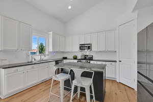 Kitchen featuring appliances with stainless steel finishes, high vaulted ceiling, white cabinets, dark stone countertops, and backsplash