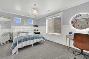 Carpeted bedroom with an office area, crown molding, wainscoting, and a decorative wall