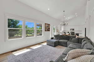 Living room with a chandelier, high vaulted ceiling, light wood finished floors, and recessed lighting