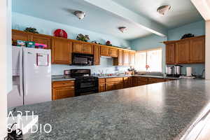 Kitchen featuring black appliances, dark countertops, brown cabinetry, and a peninsula