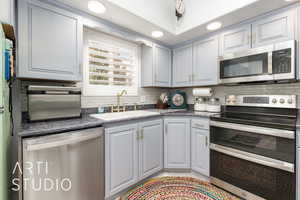 Kitchen featuring stainless steel appliances, backsplash, and dark countertops