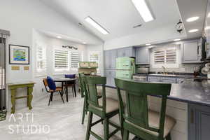 Kitchen with freestanding refrigerator, dark countertops, gray cabinetry, lofted ceiling, and decorative backsplash