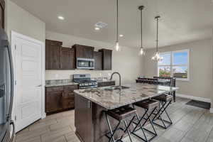 Kitchen with appliances with stainless steel finishes, a kitchen breakfast bar, a chandelier, light stone countertops, and dark brown cabinets