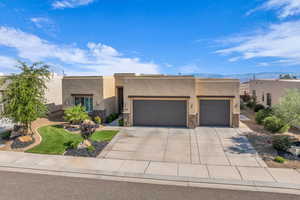 Pueblo-style home with an attached garage, stucco siding, stone siding, and driveway