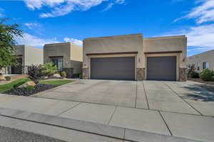 Southwest-style home featuring an attached garage, driveway, stucco siding, and stone siding