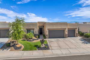 Pueblo revival-style home featuring a garage, stone siding, concrete driveway, stucco siding, and a front yard