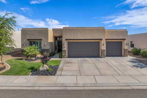 Pueblo-style house featuring a garage, stucco siding, concrete driveway, and stone siding
