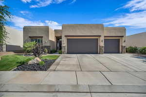 Adobe home with an attached garage, stucco siding, concrete driveway, and stone siding