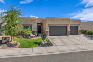 Pueblo-style home with stone siding, an attached garage, stucco siding, driveway, and a front yard