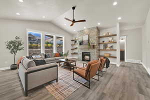 Living room featuring vaulted ceiling, ceiling fan, a stone fireplace, light wood-type flooring, and recessed lighting