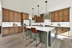 Kitchen with a center island with sink, hanging light fixtures, backsplash, stainless steel appliances, and a breakfast bar