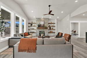 Living area featuring vaulted ceiling, a stone fireplace, light wood-style floors, ceiling fan, and recessed lighting