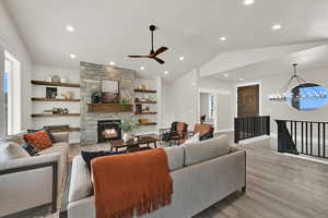 Living area with wood finished floors, lofted ceiling, a ceiling fan, recessed lighting, and a stone fireplace