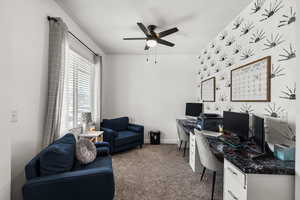 Carpeted office space with a ceiling fan and baseboards