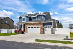 Craftsman house with a gate, concrete driveway, stone siding, an attached garage, and roof with shingles