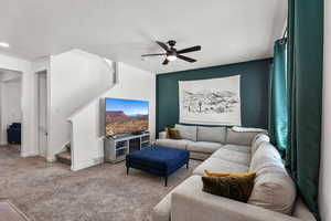 Carpeted living room with a ceiling fan, stairs, and a textured ceiling