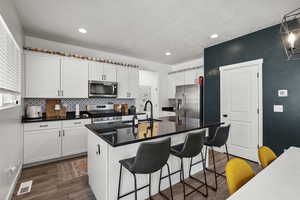 Kitchen featuring stainless steel appliances, dark wood finished floors, white cabinets, decorative backsplash, and recessed lighting