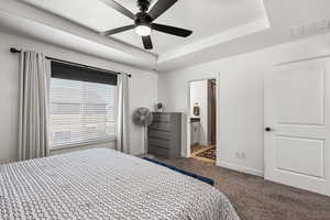 Bedroom with carpet floors, a tray ceiling, a textured ceiling, connected bathroom, and ceiling fan