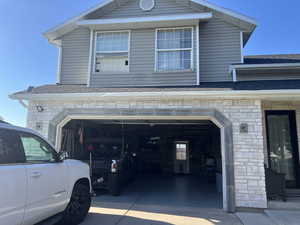 View of property exterior featuring driveway, stone siding, roof with shingles, and a garage