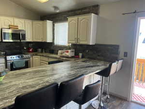 Kitchen featuring appliances with stainless steel finishes, tasteful backsplash, white cabinets, lofted ceiling, and a breakfast bar area