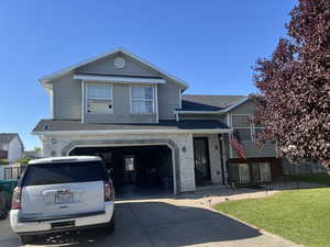 View of front of property featuring an attached garage, concrete driveway, a shingled roof, and a front yard