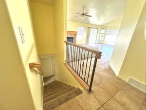 Staircase with lofted ceiling, tile patterned floors, ceiling fan, and a tiled fireplace