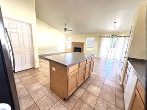 Kitchen with a ceiling fan, plenty of natural light, a kitchen island, a tile fireplace, and vaulted ceiling