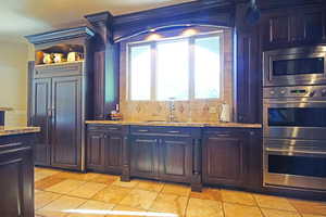 Kitchen featuring built in appliances, stone tile flooring, light stone countertops, and tasteful backsplash