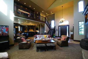 Carpeted living room featuring high vaulted ceiling, healthy amount of natural light, a chandelier, stairs, and recessed lighting