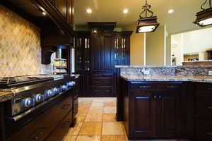 Kitchen with stainless steel gas cooktop, stone tile flooring, decorative backsplash, recessed lighting, and glass insert cabinets