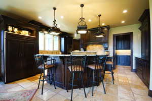 Kitchen with recessed lighting, backsplash, a kitchen bar, light stone counters, and pendant lighting