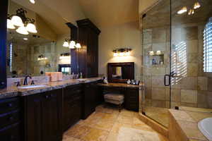 Bathroom featuring a stall shower, double vanity, a bath, stone tile floors, and lofted ceiling