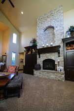 Living area featuring carpet flooring, a stone fireplace, high vaulted ceiling, and a ceiling fan
