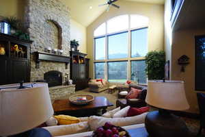 Living area with high vaulted ceiling, ceiling fan, and a stone fireplace