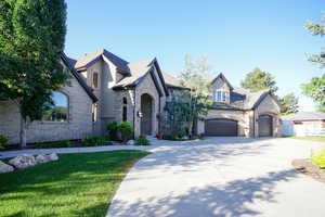 French country home featuring driveway, a front yard, an attached garage, and stone siding