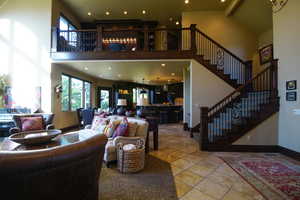 Living area with a high ceiling, healthy amount of natural light, stairs, recessed lighting, and stone tile floors