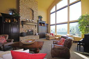 Carpeted living area featuring high vaulted ceiling and a stone fireplace