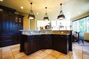 Kitchen featuring stone tile flooring, recessed lighting, light stone counters, decorative light fixtures, and glass insert cabinets