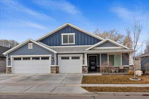 Craftsman house featuring board and batten siding, stone siding, covered porch, and driveway