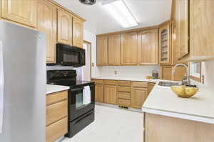 Kitchen featuring black appliances, glass insert cabinets, light countertops, and light brown cabinetry