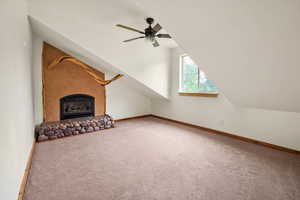 Unfurnished living room with carpet floors, a ceiling fan, a fireplace with raised hearth, and vaulted ceiling