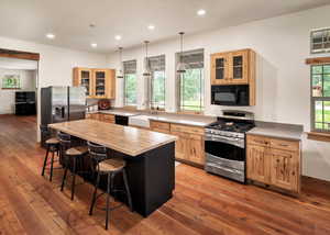 Kitchen with black appliances, light brown cabinets, a breakfast bar, butcher block counters, and hardwood / wood-style flooring